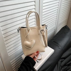 Chic beige crossbody phone bag with heart charm on a minimalist studio background