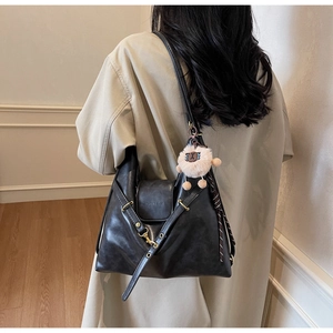 Detailed back view of a black tote bag with plush charm on a model in a warm room