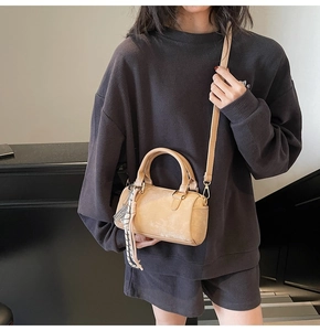 Beige Boston bag with braided charm, carried by model in a casual grey outfit