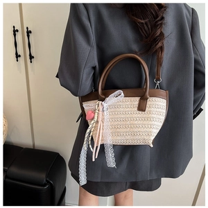 Dettaglio borsa tote in paglia intrecciata con manici in pelle marrone e fiocco in pizzo