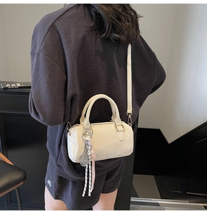 Detail of a beige cylinder boston bag featuring a unique tennis racket charm and strap