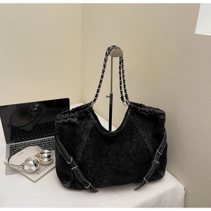Detail of black denim tote bag with chain strap and drawstring closure in casual setting