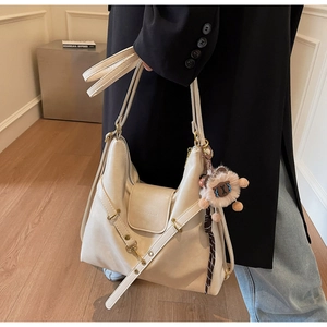 Detail of cream tote bag with gold hardware and a cute plush lion charm accessory