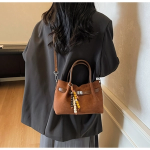 Détail du sac seau en daim marron avec pompon bohème et fermoir rotatif argenté