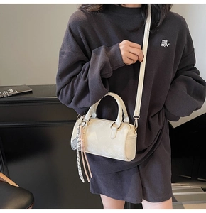 Detail view of white Boston bag with mini tennis racket charm and crossbody strap worn on side