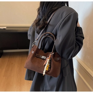 Détail du sac fourre-tout en daim marron café avec pompons ethniques et anses en cuir