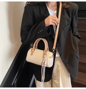 Detail of a creamy white Boston bag with brown handles and a stylish striped tassel charm