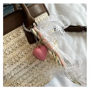 Dettaglio della borsa in paglia intrecciata con ciondolo a cuore rosa e manico in pelle