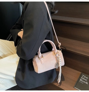 Detail view of pink suede Boston bag with metallic leaf charm and striped ribbon accent