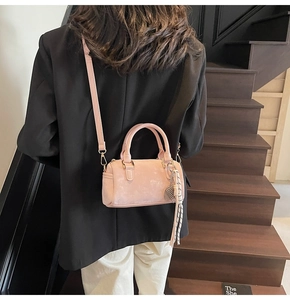 Pale pink Boston bag with woven tassel detail shown on a modern wooden staircase