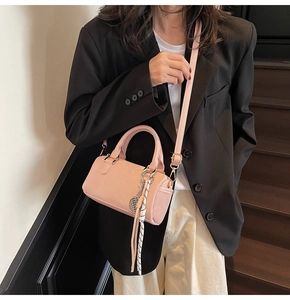 Pink Boston bag made of smooth faux leather shown worn on shoulder by a model indoors