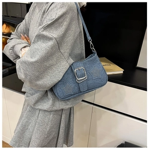 Detail of blue denim shoulder bag featuring star rivet accents and a metal buckle strap