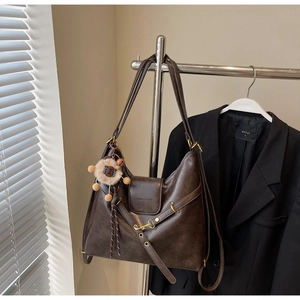 Detail of a dark brown vintage tote bag with embossed fashion text and plush charm