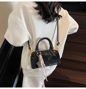 Detail of black Boston bag with metal abacus pendant and textured matte finish on straps