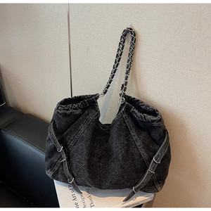 Detail of heavy washed denim tote bag with silver chain strap and decorative side laces