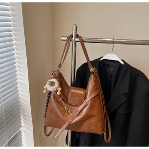Close-up of brown tote bag with lion plush charm and decorative metal buckle details