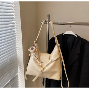 Detail of off-white leather crescent tote bag with metal buckle and plush animal charm