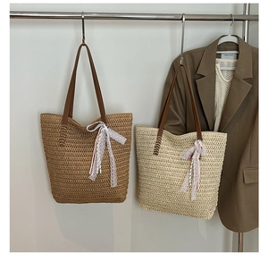 Detail of woven straw tote bag featuring leather handles and delicate lace bow charm