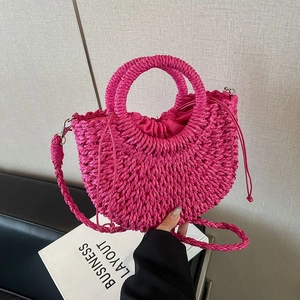 Handmade magenta straw bag in half-moon shape with ring handles and woven shoulder strap