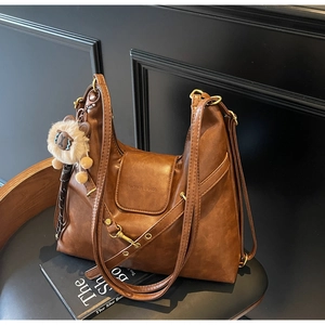 Detailed close-up of brown faux leather tote bag with lion pendant on a leather chair
