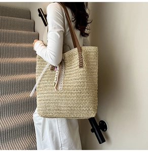 Detail of beige straw tote bag with brown leather straps and colorful beaded tassels