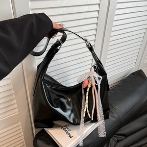Schwarze Hobo-Tasche aus glänzendem Leder mit Schleife und Herzanhängern auf Sofa