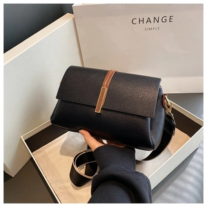 Détail du sac en cuir noir avec boucle dorée et bandoulière tissée sur boîte cadeau