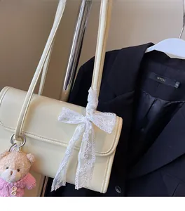 Détail du sac à bandoulière en cuir crème avec nœud en dentelle et charm ours rose