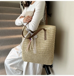 Close-up of woven straw tote bag with brown leather straps and lace bow charm