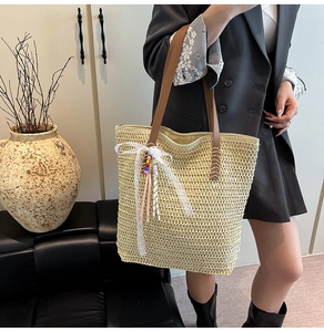 Detailed close-up of woven straw tote bag with elegant lace bow and tassel accents