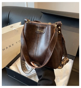 Close-up of retro brown bucket bag with textured leather and wide woven shoulder strap
