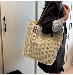 Detail of woven straw tote bag featuring white lace bow and brown leather shoulder strap