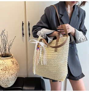 Detail of woven straw tote bag featuring brown leather straps and beaded bow charm