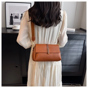 Détail d'un sac marron en cuir grainé avec large bandoulière et boucle dorée chic