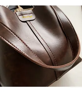 Close-up showing the soft synthetic leather texture and golden logo on the brown tote bag