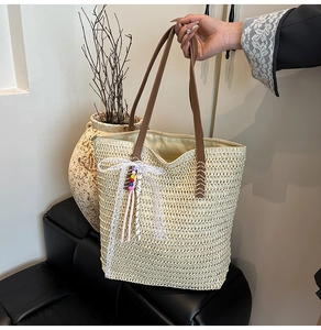 Detail view of woven straw tote bag with brown faux leather strap and white lace bow