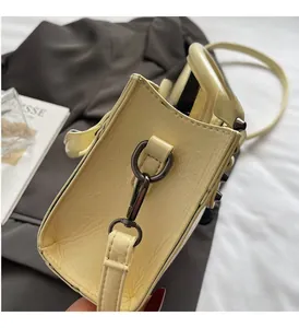 Détail d'un sac à main en cuir jaune clair avec des rivets foncés et la bandoulière
