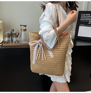 Detailed close-up of straw woven tote bag featuring white lace bow and beaded tassel
