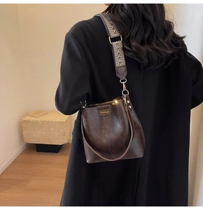 Detail of vintage brown bucket bag with geometric wide strap on black coat