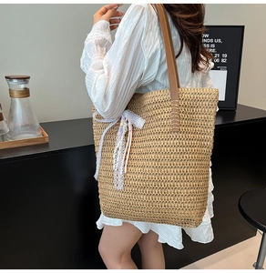 Detailed close-up of woven straw tote with white lace bow and brown leather handles