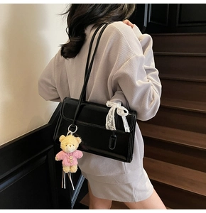 Détail du sac à bandoulière en cuir verni noir avec nœud en dentelle et pendentif ours