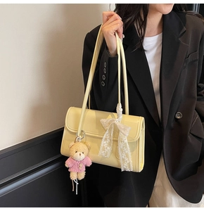 Détail d'un sac à bandoulière beige clair avec breloque ours et nœud en dentelle blanche