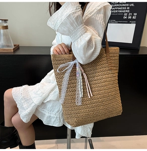 Straw tote bag detail with white lace bow and colorful woven tassel charm on leather strap