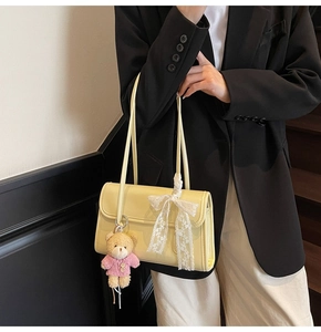 Détail du sac à bandoulière crème avec nœud en dentelle et breloque ours en peluche