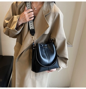 Detail of black leather bucket bag with wide geometric strap and golden logo