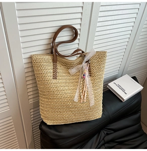 Close-up of woven straw tote bag with brown PU straps and decorative lace bow charm