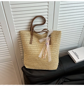 Detail view of woven straw tote bag with brown leather handles and decorative lace tassel