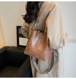 Brown leather bucket bag with vintage style and geometric woven wide shoulder strap
