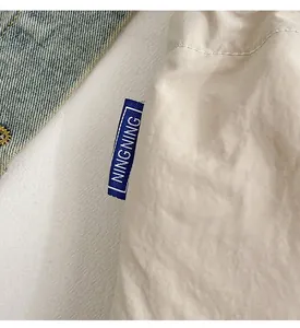 Detail of a beige nylon bag showing a navy blue woven label with subtle fabric textures