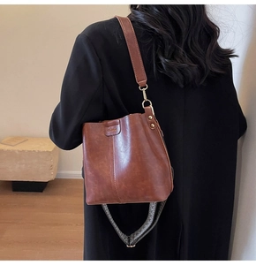 Detail of brown PU leather bucket bag featuring a woven wide strap and golden hardware